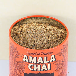 Close-up, top-down view of an open orange tin of Amala Chai Cardamom Chai Masala, revealing the loose-leaf tea and spice blend inside.