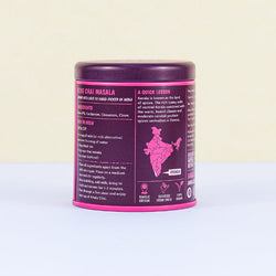 Side view of a magenta and dark purple tin of Amala Chai Rose Chai Masala showing ingredients, brewing instructions, and information about its origin in Kerala, India.