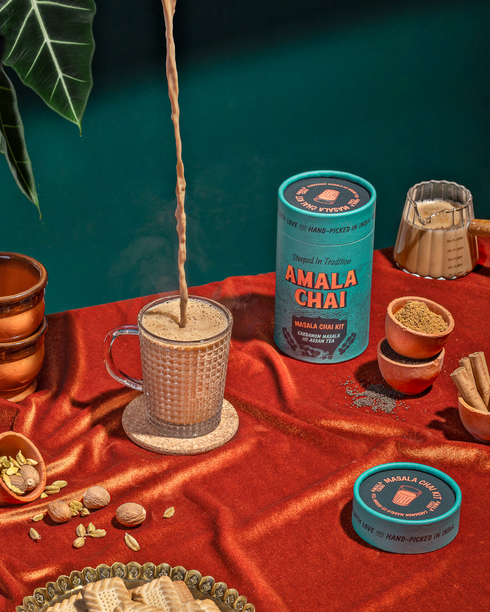 Masala Chai being poured from height into a cup with ingredients like cardamom and cinnamon strewn around