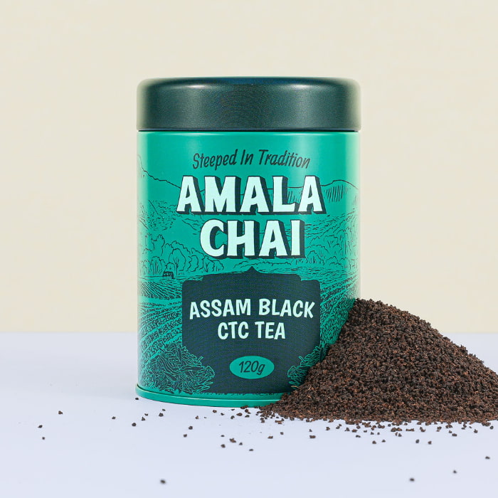 Teal tin of Amala Chai Assam Black CTC Tea with white lettering and tea field illustrations, next to a pile of dark brown CTC tea granules.