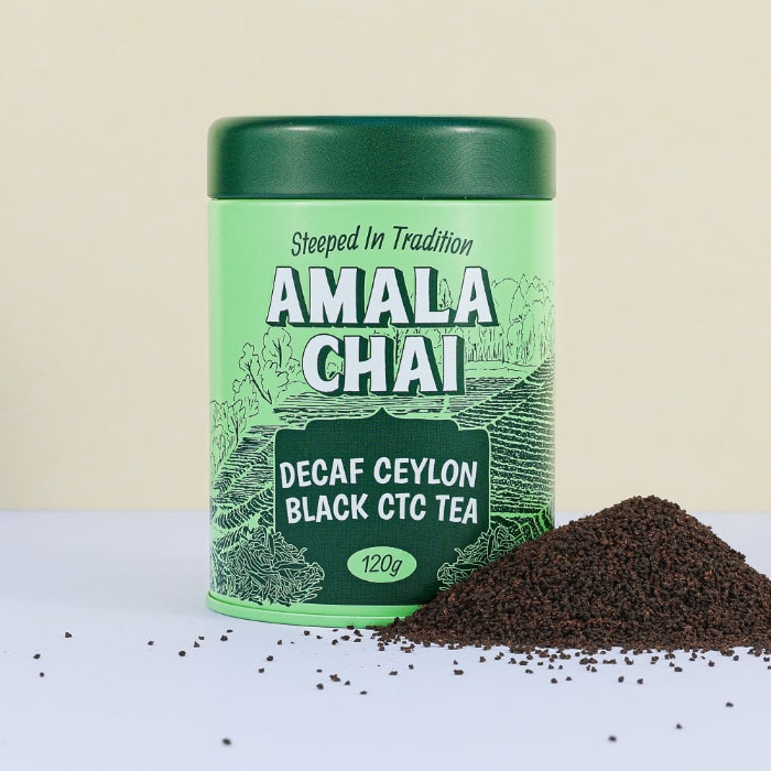 Light green tin of Amala Chai Decaf Ceylon Black CTC Tea with dark green lettering and tea field illustrations, next to a pile of dark brown decaffeinated CTC tea granules.